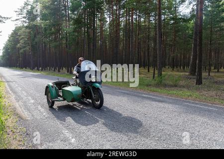 Localo auf einem alten russischen Motorrad (Motorrad) mit Beiwagen auf einer geraden Straße umgeben von Kiefernwäldern auf der Insel kihnu in der ostsee, estland Stockfoto