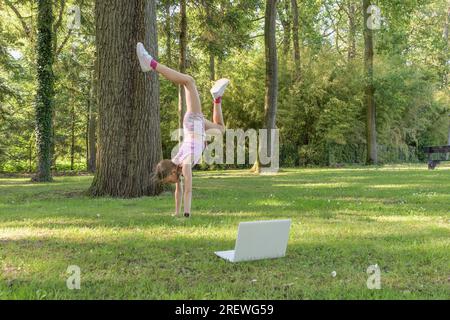 Ein Teenager führt online akrobatische Übungen durch und trainiert mit einem Computer im Park. Stockfoto