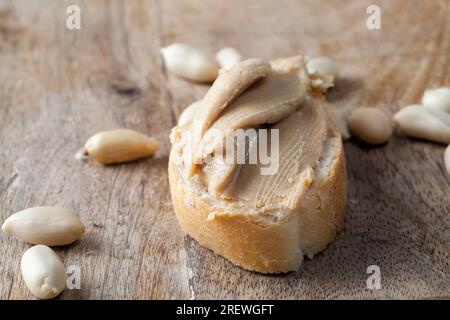 Zutaten für die Zubereitung eines schnellen Frühstücks mit Brot und Erdnüssen, Erdnusspaste geröstete Erdnüsse, köstliche Erdnussbutter und Weißbrot auf dem Tisch, Stockfoto