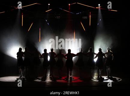 Dunkle Silhouetten tanzender Mädchen vor dem Hintergrund von weißem Licht aus Lampenlichtern. Stockfoto