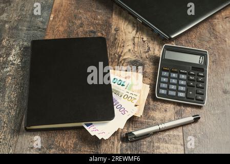 Buchfragment eines Kontogeräts mit Euro-Banknoten und einem Füllfederhalter auf einem Holztisch. Stockfoto