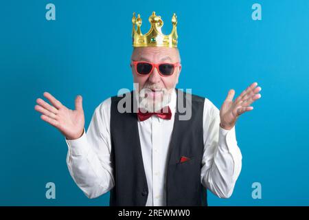 Ein lustiger alter Mann in einem festlichen Anzug mit einer Fliege und einer goldenen Krone auf dem Kopf Stockfoto