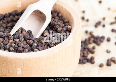 Gewürz schwarzer Pfeffer auf einem alten Holztisch in der Küche verstreut, werden duftende schwarze Pfeffererbsen beim Kochen während der Zubereitung von Fleisch verwendet Stockfoto