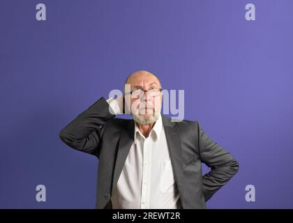 Porträt eines älteren Mannes mit Bart und Brille, blickt mit Bedacht auf. Platz für Text. Violetter Hintergrund Stockfoto