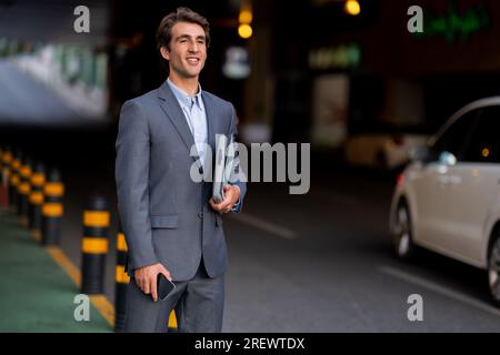 Ein hübscher Geschäftsführer, der am Parkplatz steht und auf das Auto wartet Stockfoto