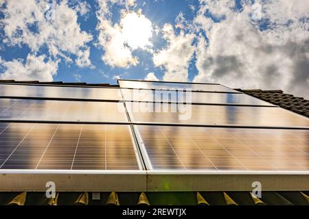 Sonnenkollektoren auf einem Hausdach in abendlicher Stimmung und Hintergrundbeleuchtung mit Wolken am Himmel, Deutschland Stockfoto