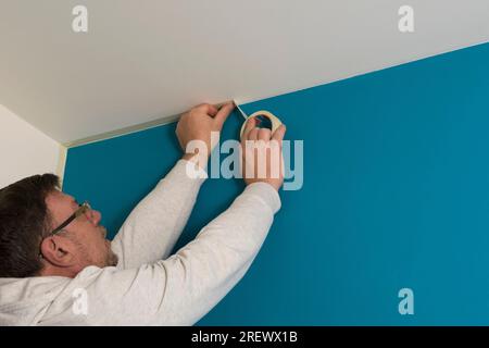 Der Mann klebt Abdeckband an die Decke, bevor er die Wand streicht Stockfoto