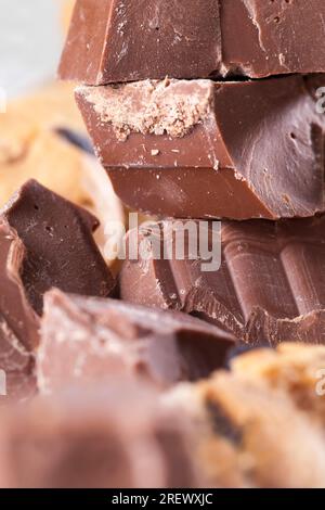 Große Stücke Milchschokolade auf dem Tisch, zerbrochene Schokolade und Weizenkekse mit Schokoladentropfen, Fastfood-Artikel, sehr kalorienreiches Kakaopulver Stockfoto