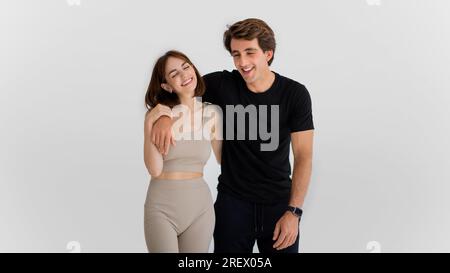 Lachender, fröhlicher junger weißer Mann, der eine Frau in Sportbekleidung umarmt, viel Spaß beim Workout Stockfoto