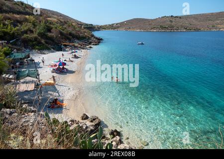 Blick auf den abgeschiedenen und idyllischen Strand in der Nähe von Porto Palermo, Albanien, mit Menschen, die schwimmen und Spaß haben. Touristen genießen den Sommer in Albanien Stockfoto