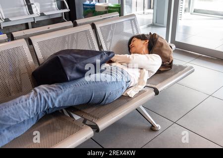 Müde Asiatin liegt flach im Wartebereich des Flughafens und wartet auf den Flug Stockfoto