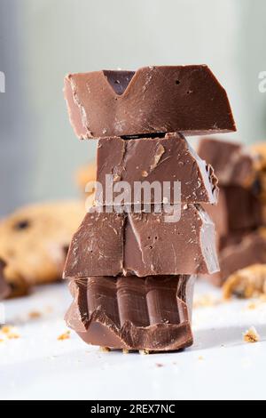 Große Stücke Milchschokolade auf dem Tisch, zerbrochene Schokolade und Weizenkekse mit Schokoladentropfen, Fastfood-Artikel, sehr kalorienreiches Kakaopulver Stockfoto