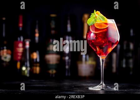 Rotes Sangria-Sommergetränk mit spanischem Rotwein, Pfirsich, Pflaume, Orange, Limette und Eis. Schwarzer Bartheke-Hintergrund, Stahlbarren und Flaschen Stockfoto