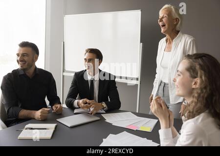 Fröhliche jüngere und ältere Kollegen treffen sich im Sitzungssaal Stockfoto