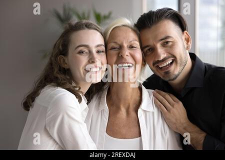 Erwachsene Geschwister umarmen die ältere Mutter, stehen mit Wangenberührungen nah Stockfoto