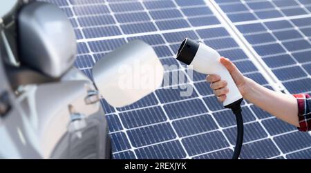 Hand mit Ladestecker für Elektrofahrzeuge auf einem Hintergrund des Solarmoduls. Stockfoto