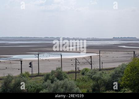 Blick auf das ausgetrocknete Kachovsky-Reservoir. Trotz der derzeit andauernden ukrainischen Gegenoffensive in der Region Zaporischzhya und der Gefahr eines Terroranschlags auf das Kernkraftwerk ist das tägliche Leben in der Region Zaporischzhien noch nicht vorbei. Die Straßen der Stadt sind an warmen Abenden mit Spaziergängern gefüllt, während die Sonnenblumen in den Außenbereichen blühen und die erste Ernte begonnen hat. Die intensivere Kriegsführung lässt jedoch nicht nach - fast täglich nehmen intensive Bombenanschläge das Leben von Menschen in Anspruch, die zusätzlich unter Wassermangel leiden, nachdem der Damm Nova Kakhovka in die Luft gesprengt wurde. Stockfoto