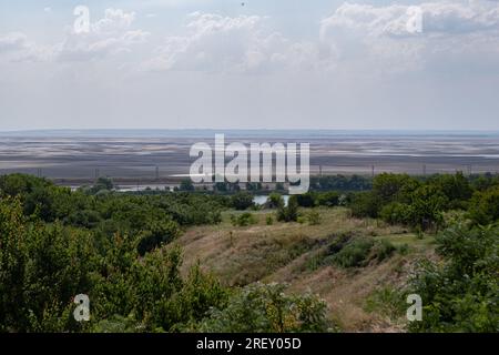 Blick auf das ausgetrocknete Kachovsky-Reservoir. Trotz der derzeit andauernden ukrainischen Gegenoffensive in der Region Zaporischzhya und der Gefahr eines Terroranschlags auf das Kernkraftwerk ist das tägliche Leben in der Region Zaporischzhien noch nicht vorbei. Die Straßen der Stadt sind an warmen Abenden mit Spaziergängern gefüllt, während die Sonnenblumen in den Außenbereichen blühen und die erste Ernte begonnen hat. Die intensivere Kriegsführung lässt jedoch nicht nach - fast täglich nehmen intensive Bombenanschläge das Leben von Menschen in Anspruch, die zusätzlich unter Wassermangel leiden, nachdem der Damm Nova Kakhovka in die Luft gesprengt wurde. Stockfoto