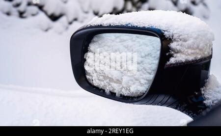 Seitenfenster des Autos im Schnee. Nahaufnahme eines mit Schnee bedeckten Außenspiegels auf weißem, schneebedeckten Boden Stockfoto