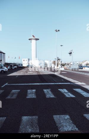 Vertikale Aufnahme eines Flughafenbereichs im Freien mit EINEM VOR-Antennenturm (UKW Omnidirektionale Reichweite), einer Asphaltstraße im Schatten mit Fußgängerüberquerung, Stockfoto