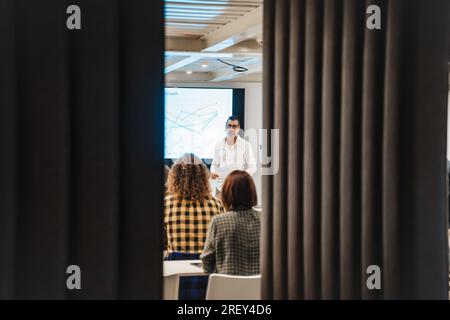 Erfahrener Lehrer mittleren Alters, der Wissen und Geschäftsideen an eine multiethnische, generationenübergreifende Unternehmensgruppe weitergibt Stockfoto