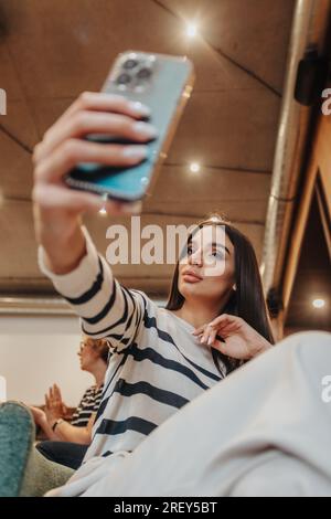 Foto einer brünetten Frau mit Handy, die während der Pause im Büro ein Selfie macht Stockfoto