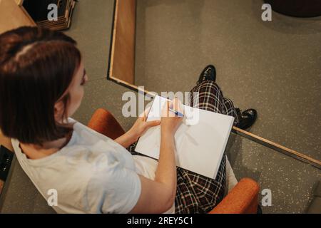 Top View-Aufnahme einer kurzhaarigen Frau, die in ein Notizbuch schreibt Stockfoto