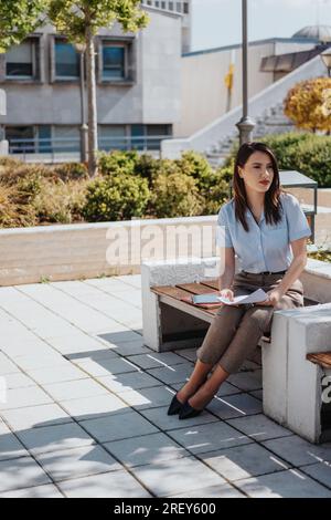 Brünette Frau, die ihrem Kollegen beim Ideenaustausch zuhört, während sie auf einer Bank sitzt. Business Outdoor-Konzept Stockfoto