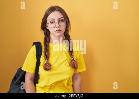 Junge weiße Frau, die einen Studentenrucksack auf gelbem Hintergrund trägt, schläfrig und müde aussieht, erschöpft wegen Müdigkeit und Kater, faule Augen im m Stockfoto