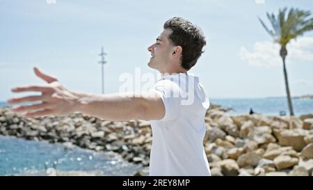 Junger lateinamerikanischer Mann atmet mit offenen Armen am Strand Stockfoto