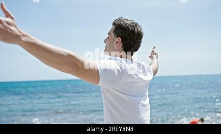 Junger lateinamerikanischer Mann atmet mit offenen Armen am Strand Stockfoto