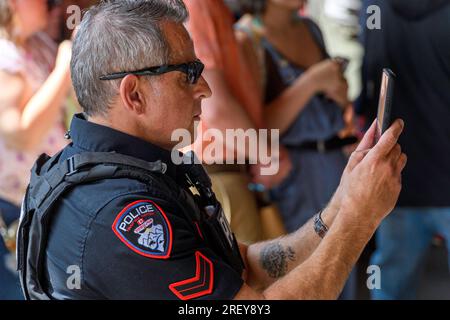 Ein Polizist der Tsuut'ina Nation, der an der Grand Entrance-Zeremonie Powwow in Bragg Creek, Alberta, Kanada teilnimmt, während er ihn mit einem Smartphone filmt. Stockfoto