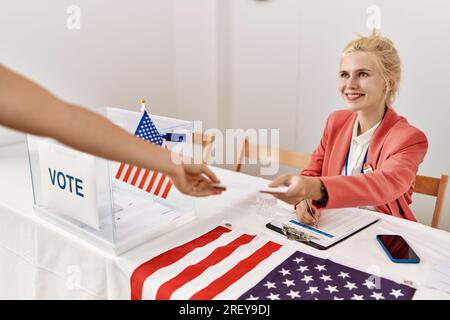 Junge blonde Frau, die Wahlpräsidentin, die auf dem Klemmbrett schreibt und an der Wahlhochschule abstimmt Stockfoto