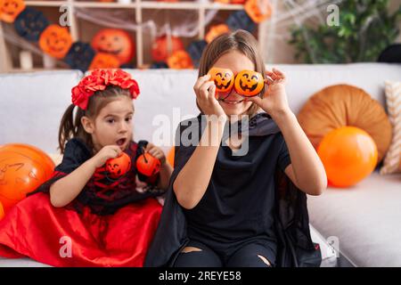 Ein süßer Junge und ein Mädchen, die halloween-Kostüme tragen und zu Hause Kürbiskörbe über die Augen halten Stockfoto