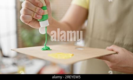 Ein junger hispanischer Künstler, der im Kunststudio Farbe auf die Palette gießt Stockfoto