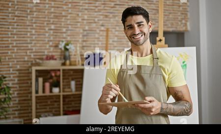 Junger hispanischer Künstler, der im Kunstatelier selbstbewusst Farben auf Farbpalette mischt Stockfoto