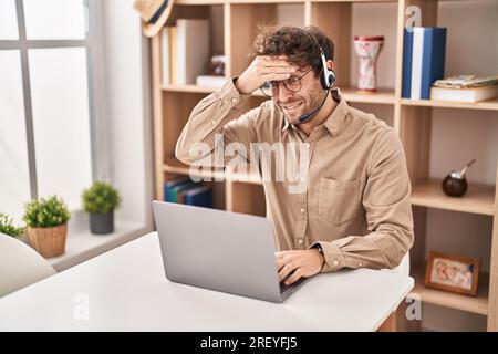 Hispanischer junger Mann mit Headset für Callcenter-Agenten, gestresst und frustriert von Hand auf Kopf, überrascht und wütend Stockfoto