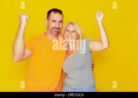 Ein echtes weißes Paar in den 40s Jahren mit erhobenen Fäusten, das erfolgreiche Action feiert, isoliert auf gelbem Hintergrund. Stockfoto