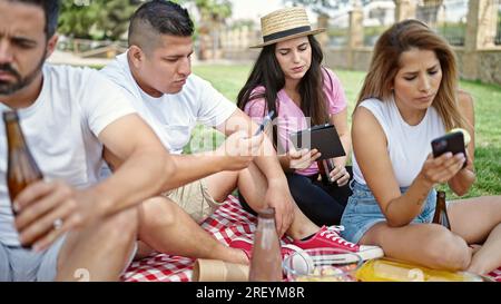 Gruppe von Personen, die ein Picknick mit Smartphones und Touchpad im Park machen Stockfoto
