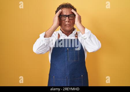 hispanischer Mann im mittleren Alter mit professioneller Kochschürze und Hand am Kopf gegen Kopfschmerz wegen Stress. Migräne leiden. Stockfoto