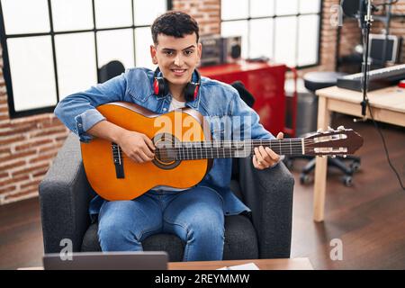 Junger nicht binärer männlicher Musiker, der klassische Gitarre im Musikstudio spielt Stockfoto