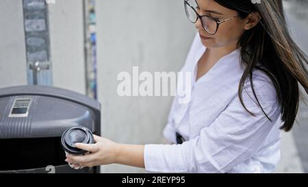 Junge, wunderschöne hispanische Frau, die Pappkaffee in den Müll wirft, in den Straßen von Madrid Stockfoto