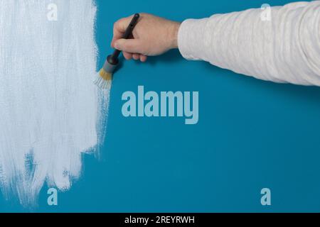 Männerhand mit Pinsel beim Malen einer blauen Wand Weiß kopieren Stockfoto