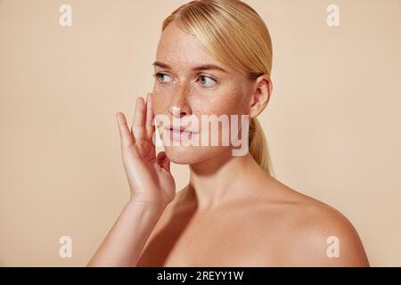 Studiofoto einer jungen Frau mit Sommersprossen, die ihr Gesicht berührten Stockfoto