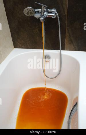 Rostiges Wasser fließt aus dem Wasserhahn in die Badewanne im Badezimmer. Die fließende Flüssigkeit aus dem Wasserhahn im Hausbad hat einen Schatten von RE Stockfoto