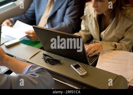 Personen, die während einer Zugfahrt an Laptops und Dokumenten arbeiten. Stockfoto