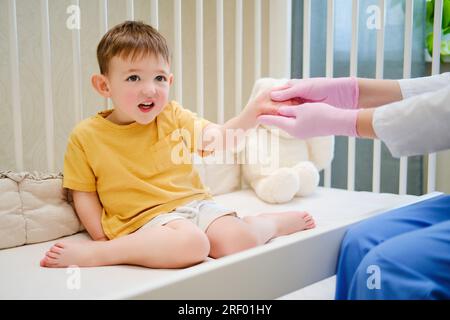 Der Arzt macht Gymnastik und eine Handmassage für ein Kleinkind. Krankenschwester in Uniform, die orthopädische Hand-Finger-Übungen beim Kind durchführt. Der Junge ist etwa zwei Jahre alt Stockfoto