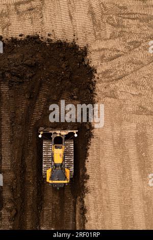 Luftaufnahme direkt über einem Bulldozer oder einer Erdbewegungsmaschine mit Raupenketten, die Erde und Boden in der Bauindustrie auf einem Brachland mit Stockfoto