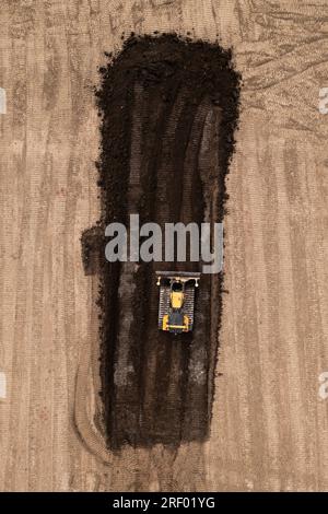 Luftaufnahme direkt über einem Bulldozer oder einer Erdbewegungsmaschine mit Raupenketten, die Erde und Boden in der Bauindustrie auf einem Brachland mit Stockfoto