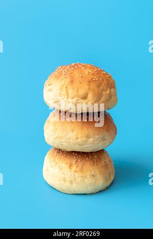 Nahaufnahme mit hausgemachten Burgerbrötchen, minimalistisch auf einem blauen Tisch. Frisch gebackene Brotbrötchen, gestapelt. Stockfoto